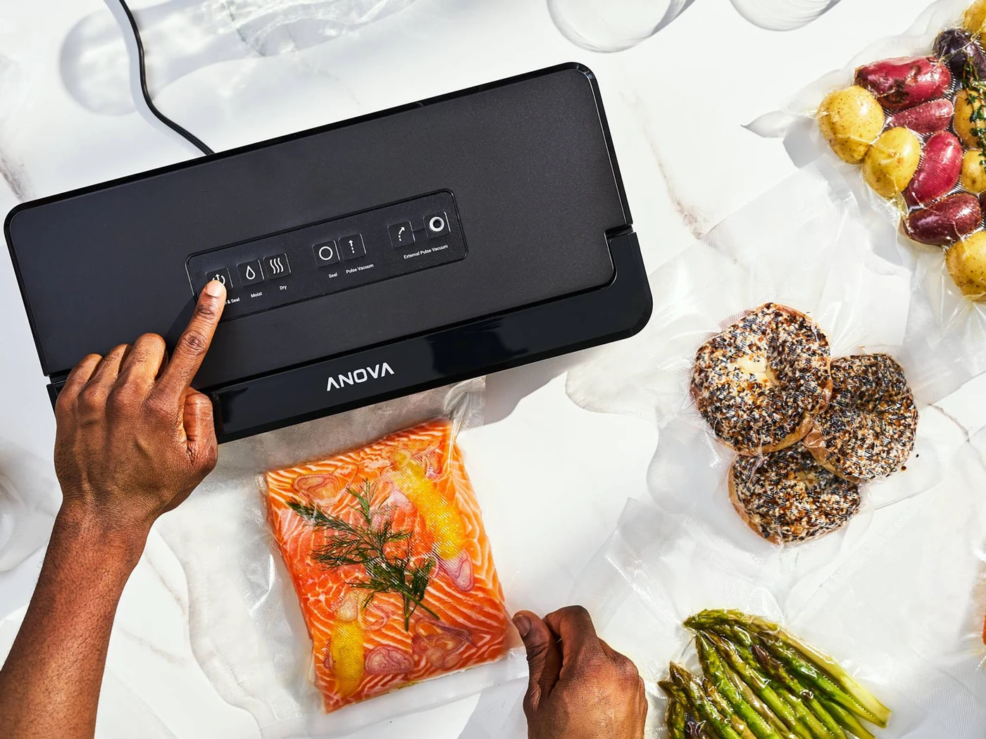 Anova Precision Vacuum Sealer Pro with a black rectangular body sealing a salmon portion on a white counter