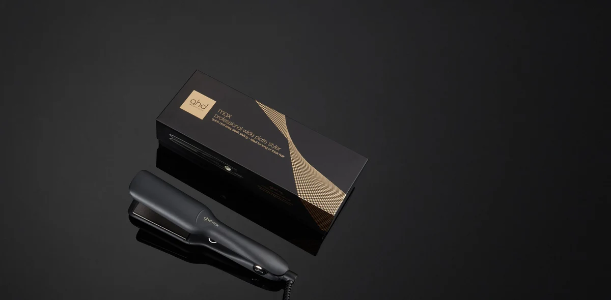 Black ghd Max wide-plate flat iron beside its manufacturer packaging
